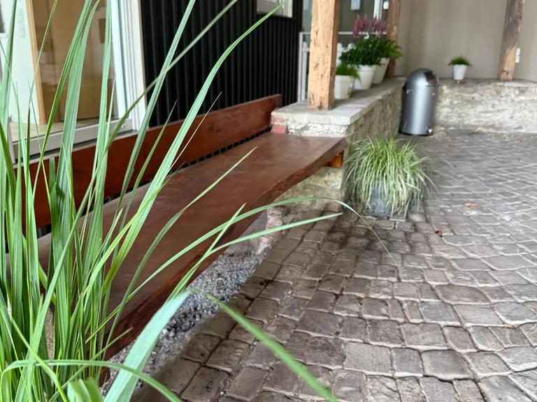 Holzbank und Naturstein im grünen Innenhof von The Greenhouse Alsbach